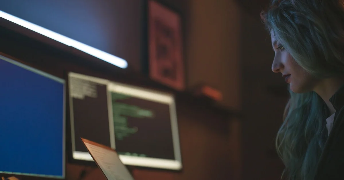 Developer in front of several screens showing code in a dimly lit office