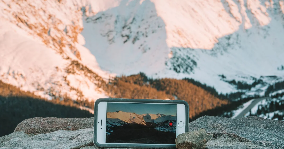 Phone resting on a rock facing snowy mountains, in a remote area far from any city
