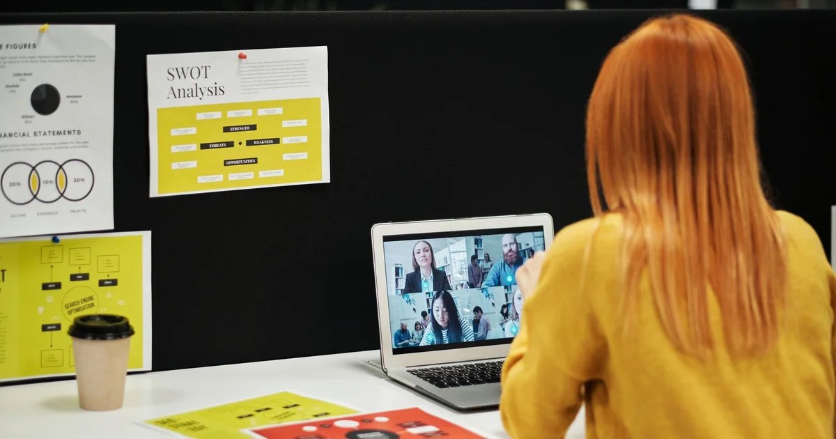 Woman on a team video call from her laptop, in front of a board with work charts