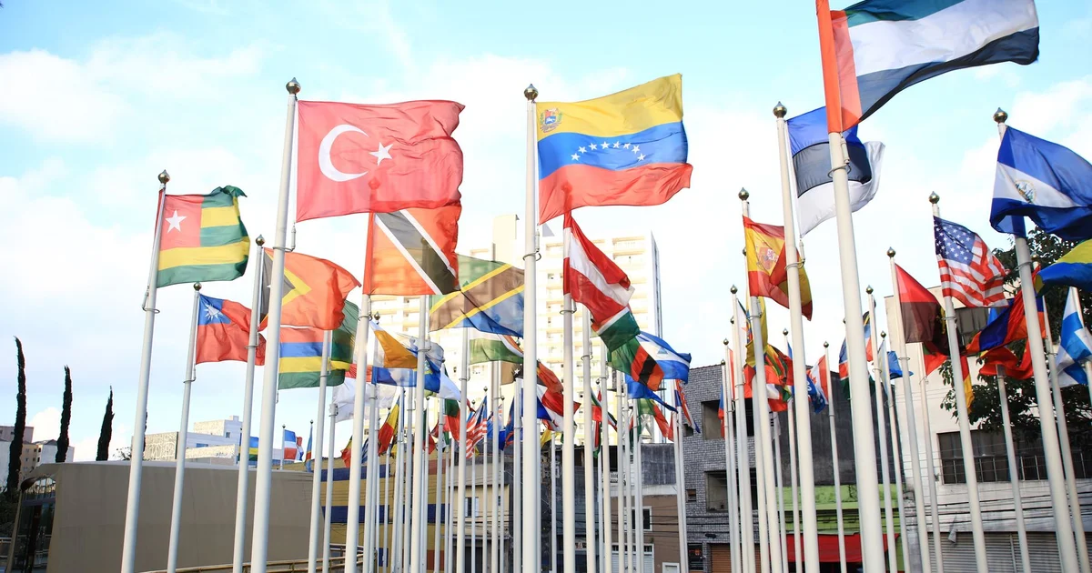 Flags of several countries flying together outdoors in a city