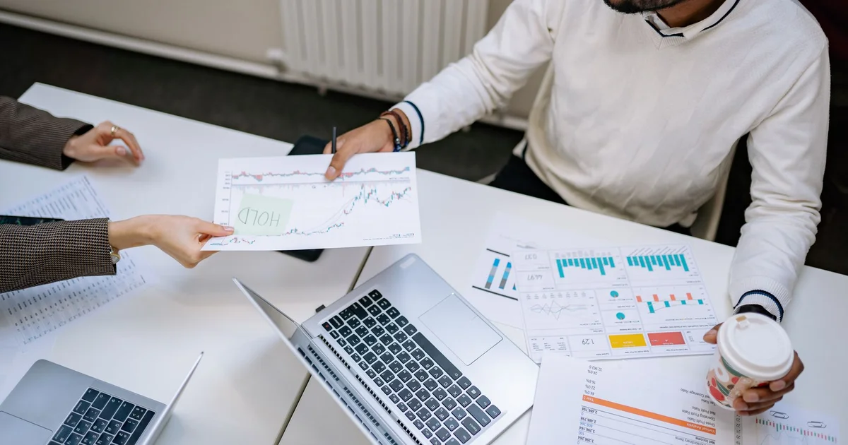 Colleagues reviewing printed financial charts next to a laptop at a meeting table