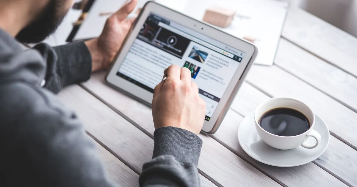 Man reading news on a tablet next to a cup of coffee