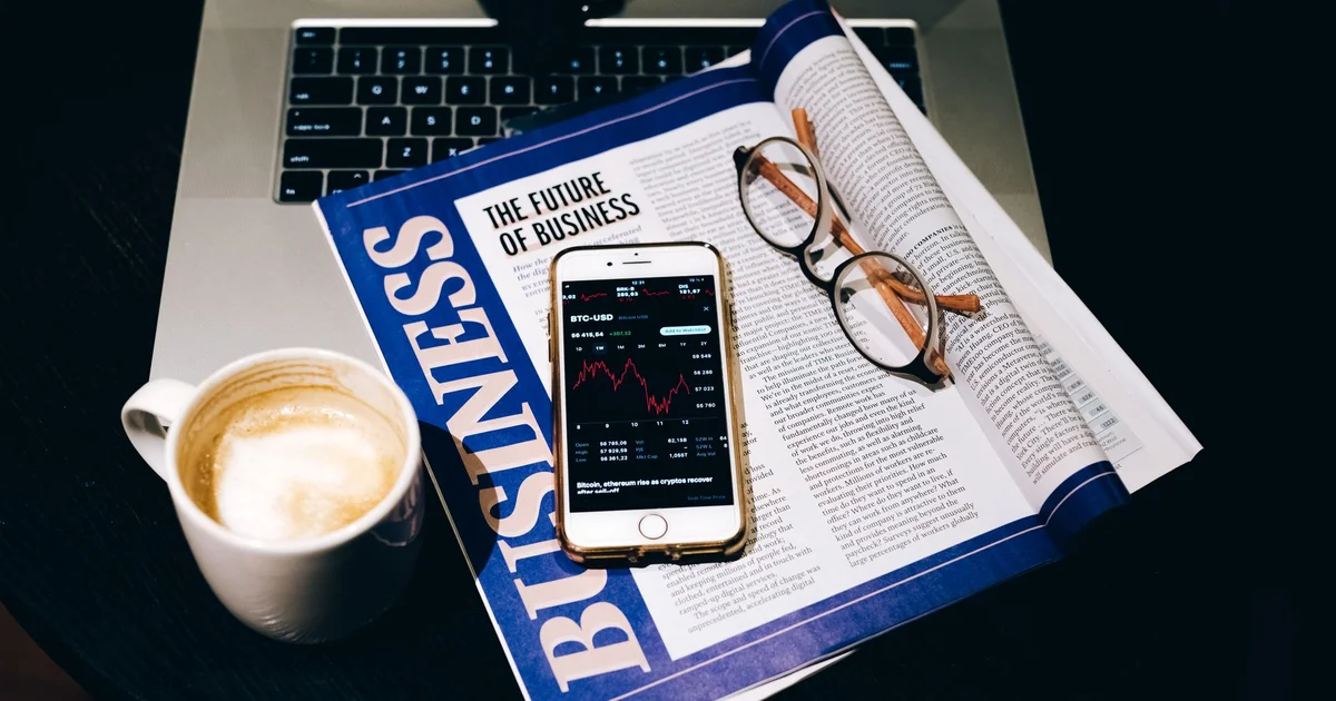 Escritorio con laptop, café, celular y un periódico de negocios