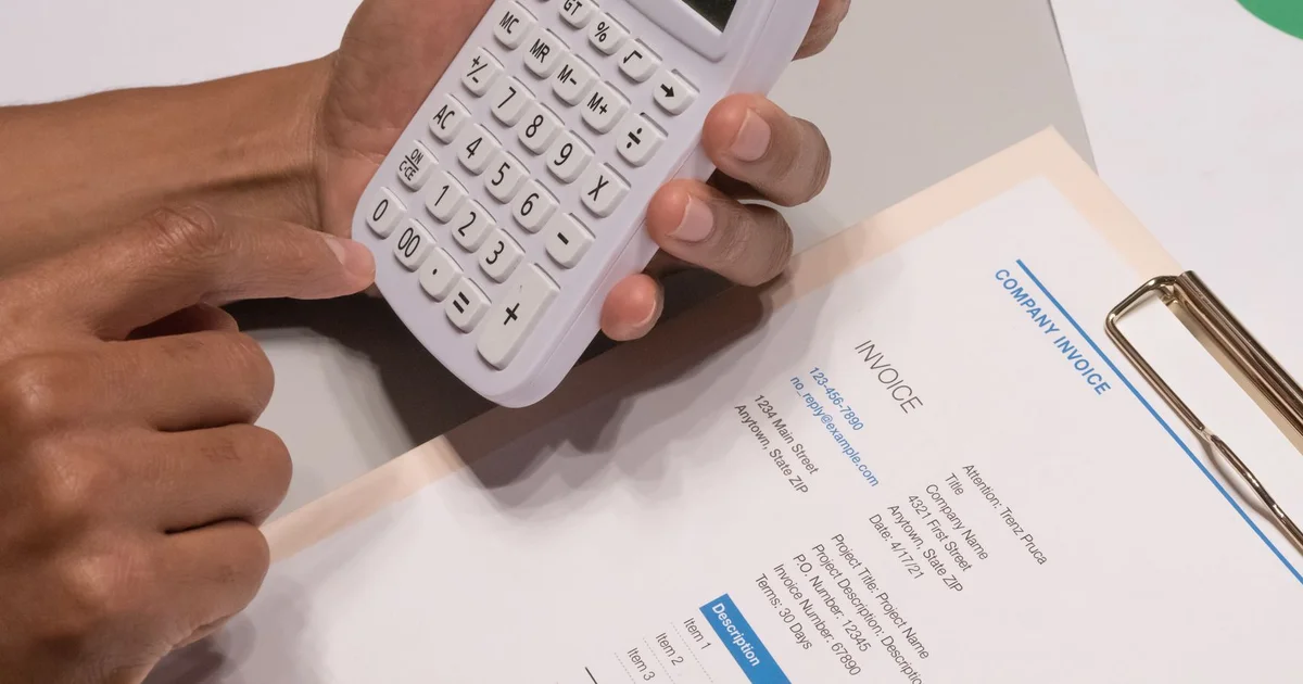 Hands using a calculator next to a printed invoice on a clipboard